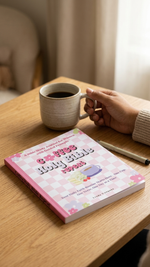 Person holding a mug with a colorful book titled 'Girl's Holy Bible' on a wooden table.