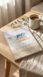 Book titled 'Girl Just Pray About It' on a wooden table with a cup of coffee and eucalyptus leaves.