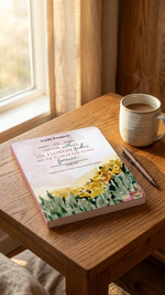 Book with a floral cover on a wooden table next to a mug of coffee and pen.